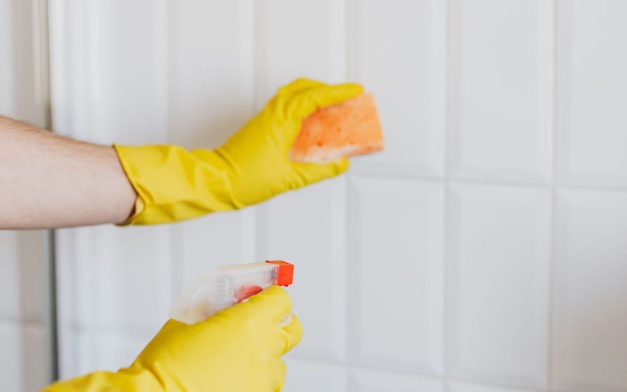 Gloved hand cleaning bathroom wall tiles with a sponge