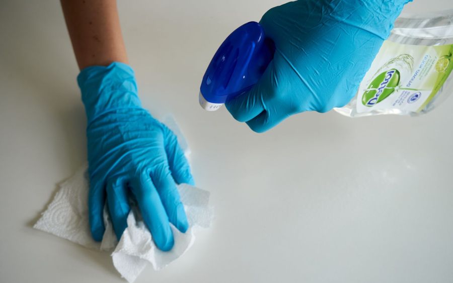 Gloved hands deep-scrubbing a surface with cleaning spray